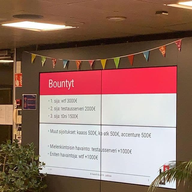 Valokuva LähiTapiola Hack Day -tapahtumasta. Seinälle heijastettu kuva, jossa teksti: "Bountyt. // - 1. sija: wtf 3000€ // - 2. sija: testausserveri 2000€ // - 3. sija: t0ni 1500€ // - Muut sijoitukset: kaaos 500€, ks-atk 500€, accenture 500€ // Mi</p>elenkiintoisin havainto: testausserveri +1000€ // - Eniten havaintoja: wtf +1000€